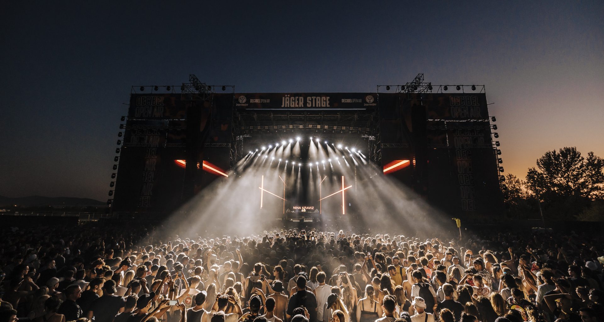 Crowd enjoying a night performance at Decibel Open Air 2024 festival with vibrant lights and a large outdoor stage.