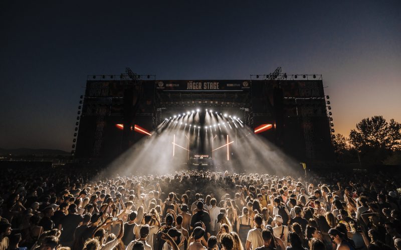 Crowd enjoying a night performance at Decibel Open Air 2024 festival with vibrant lights and a large outdoor stage.