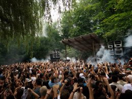 A large crowd dances energetically under the canopy of trees at Dekmantel 2024, creating an immersive festival atmosphere