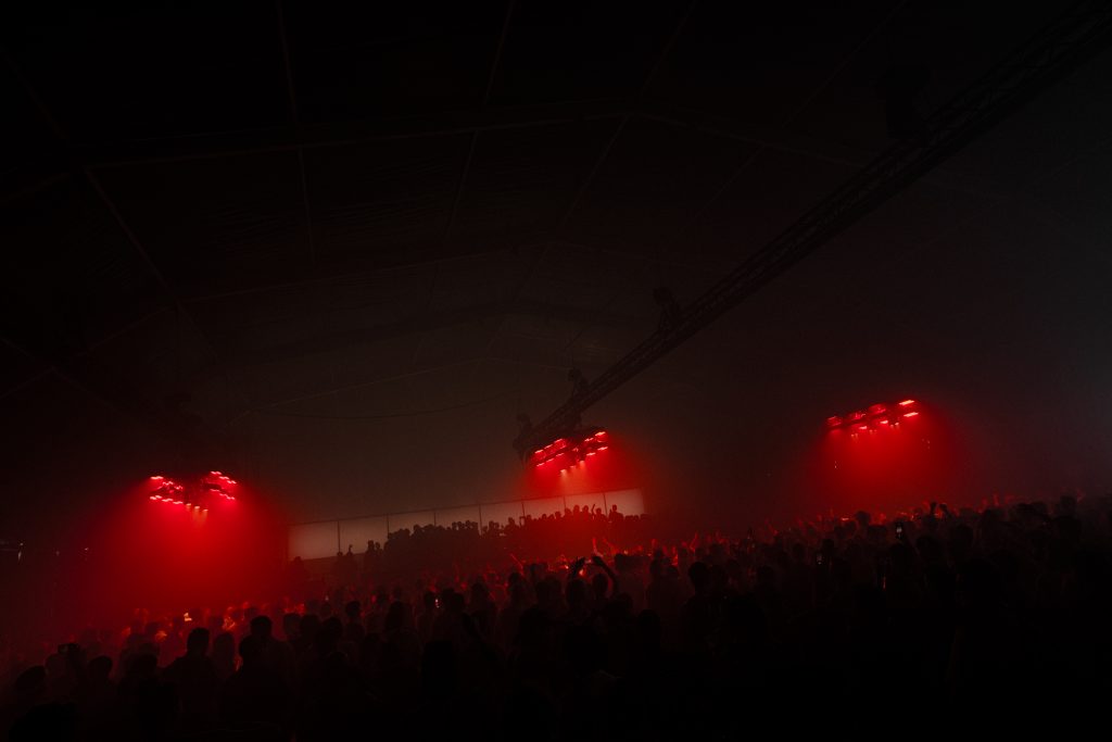 A dark, atmospheric indoor stage bathed in red light at Dekmantel 2024, filled with silhouettes of dancing festival attendees.