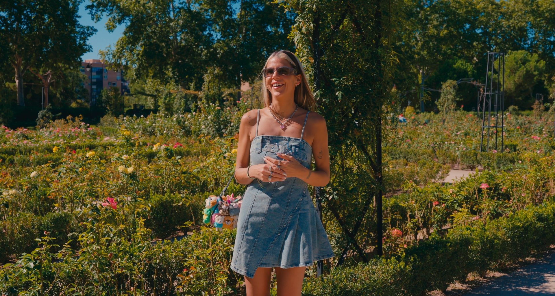 Woman standing outdoors in a garden, smiling during an interview Otta, wearing a denim dress and sunglasses