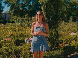 Woman standing outdoors in a garden, smiling during an interview Otta, wearing a denim dress and sunglasses