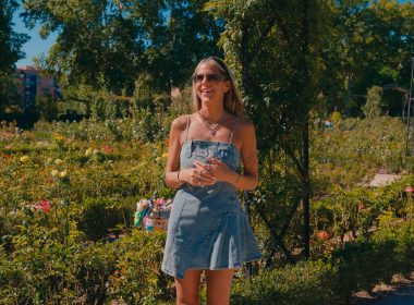 Woman standing outdoors in a garden, smiling during an interview Otta, wearing a denim dress and sunglasses