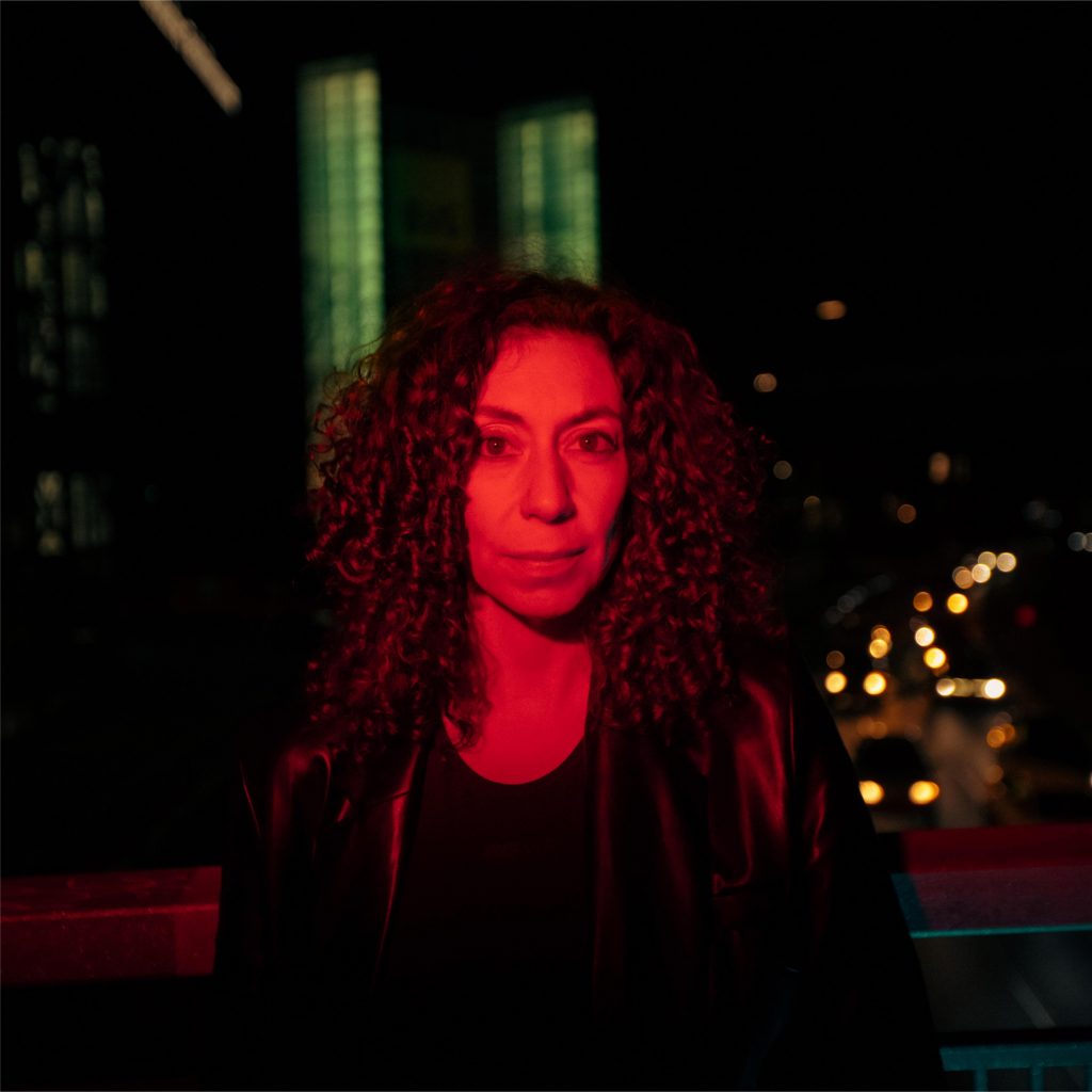 Andrea Rosen standing with red lighting and city lights in the background, highlighted by XCEED for electronic music trends 2025