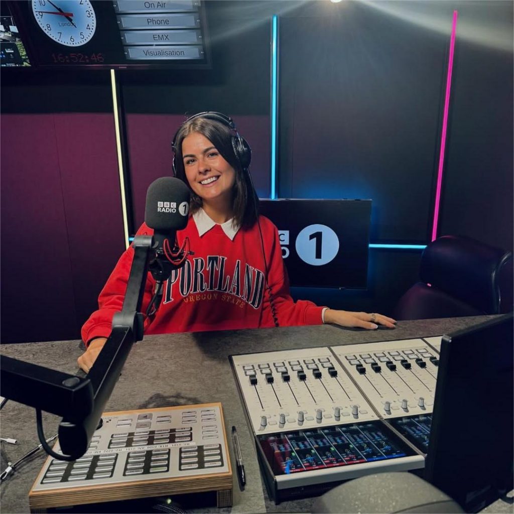 Katie Knight in a BBC radio studio wearing a red sweatshirt and headphones, featured in XCEED’s electronic music trends 2025 insights